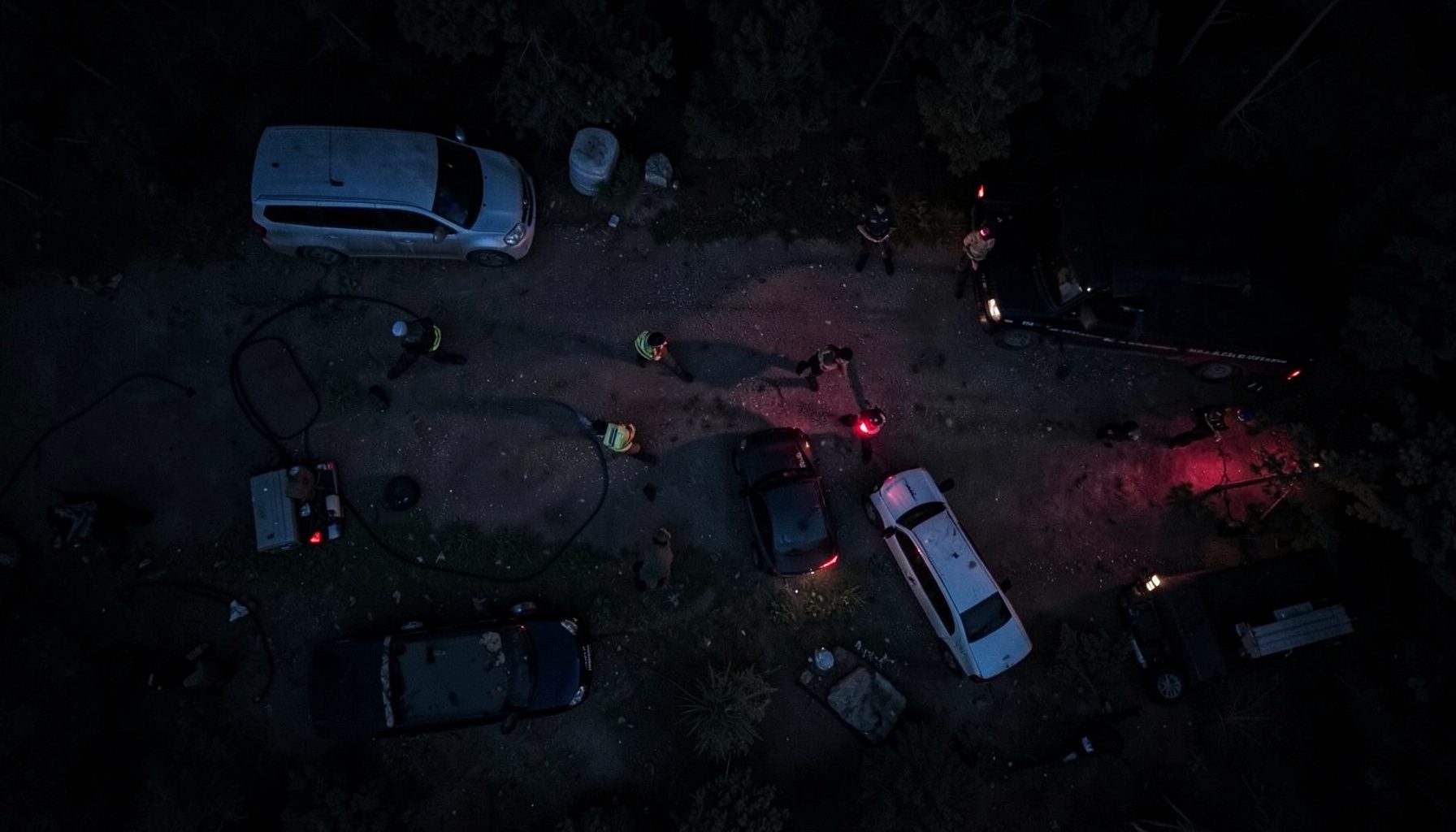 Jandarma ekiplerinin gece operasyonunda araç ve ekipmanlarla yol kontrolü yaptığı, mavi ve kırmızı ışıkların yansıdığı karanlık bir kırsal alan